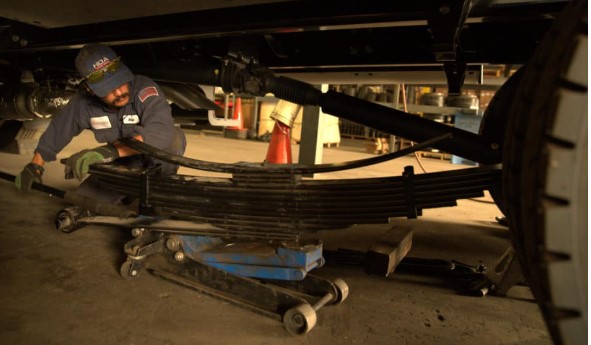 Palmer Spring Company technician repairing a heavy-duty leaf spring with a floor jack